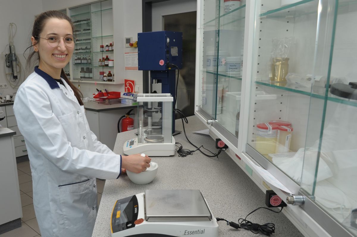 Eine Mitarbeiterin der Babelsberg Apotheke in Potsdam steht im Labor, hält einen Mörser und verarbeitet Zutaten zur Herstellung einer Rezeptur.