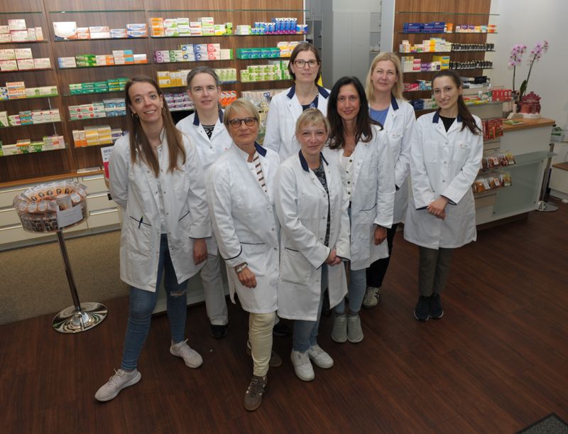 Team der Babelsberg Apotheke in Potsdam Acht Mitarbeiterinnen der Babelsberg Apotheke in Potsdam stehen gemeinsam im Verkaufsraum vor den Arzneimittelregalen und lächeln in die Kamera.